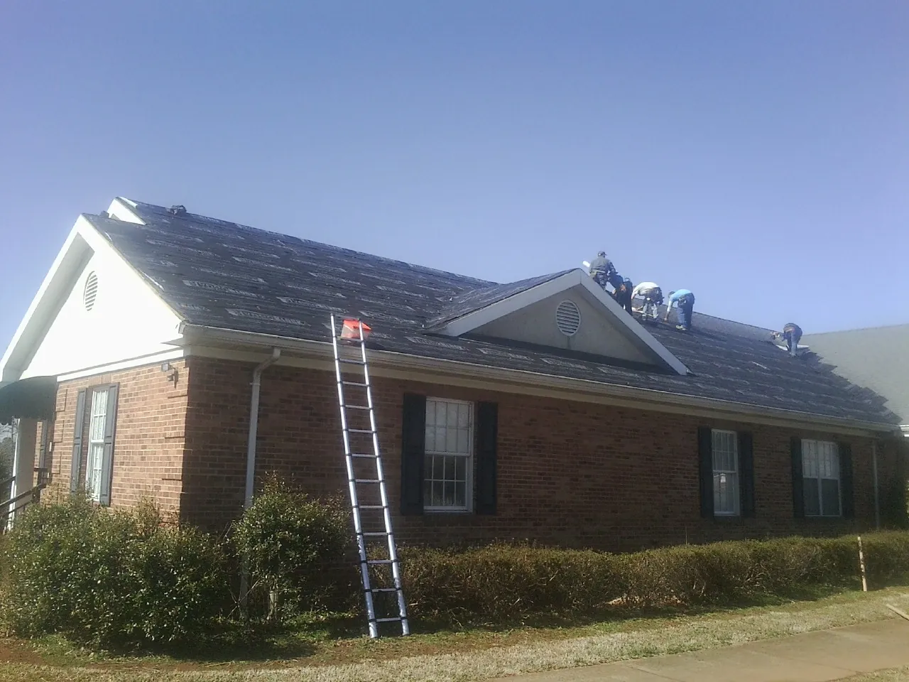 Crew tearing shingles off a brick ranch roof with a ladder set — Emergency Roof Repair work by our crew in Havre De Grace