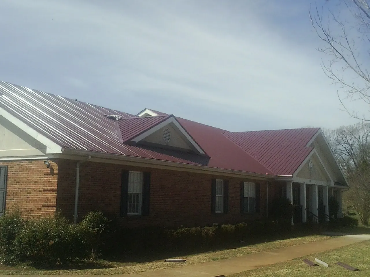 Red metal roof with gabled entries on a long brick building, from a Hail Damage Roof Repair job in Havre De Grace