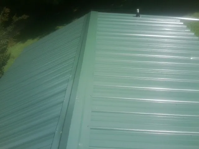 New green metal panels meeting at the ridge of a roof — Flat Roof Repair work by our crew in Havre De Grace