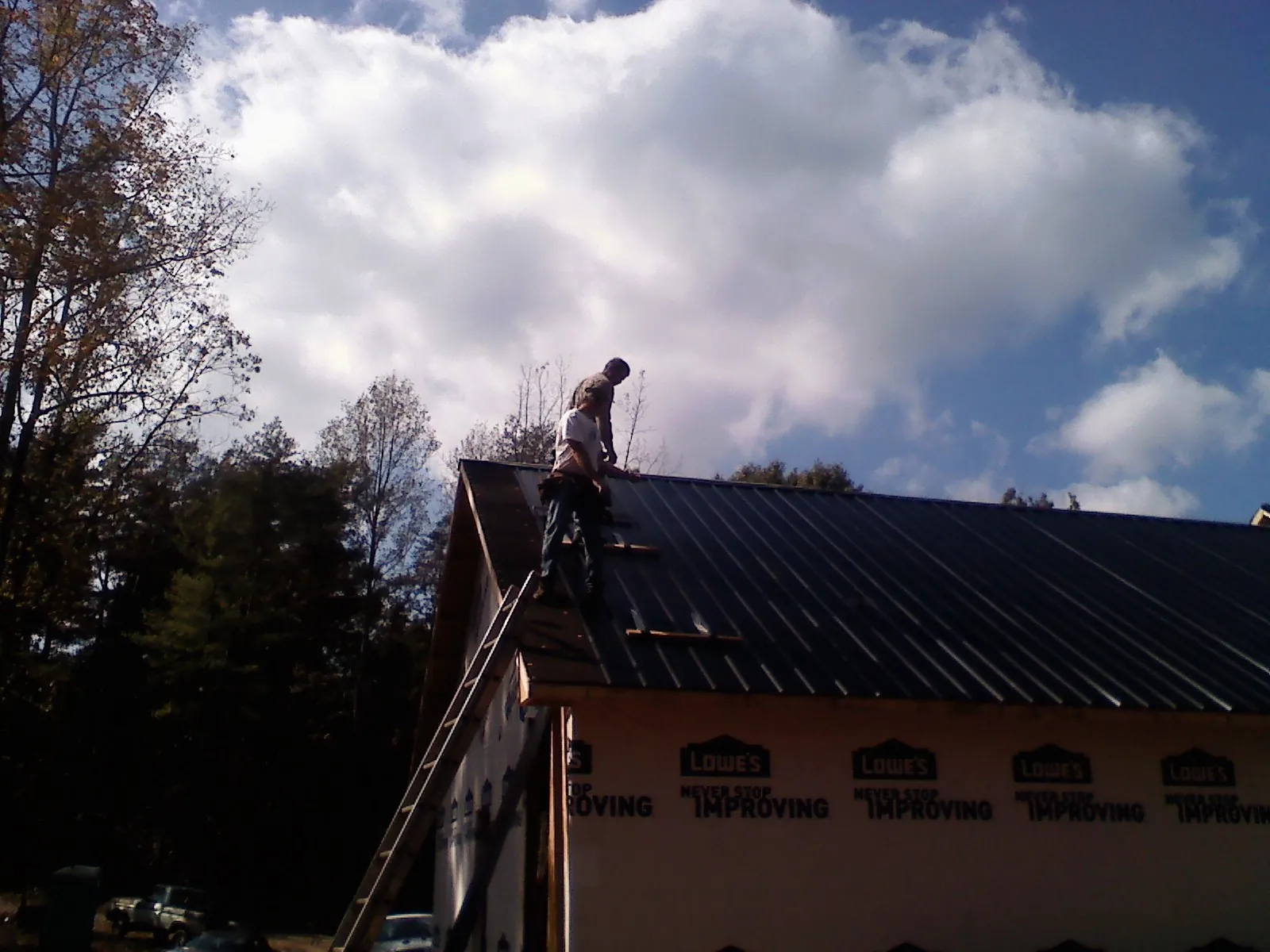 Roofer fastening dark metal panels high against a cloudy sky, from a Roof Inspection job in Havre De Grace