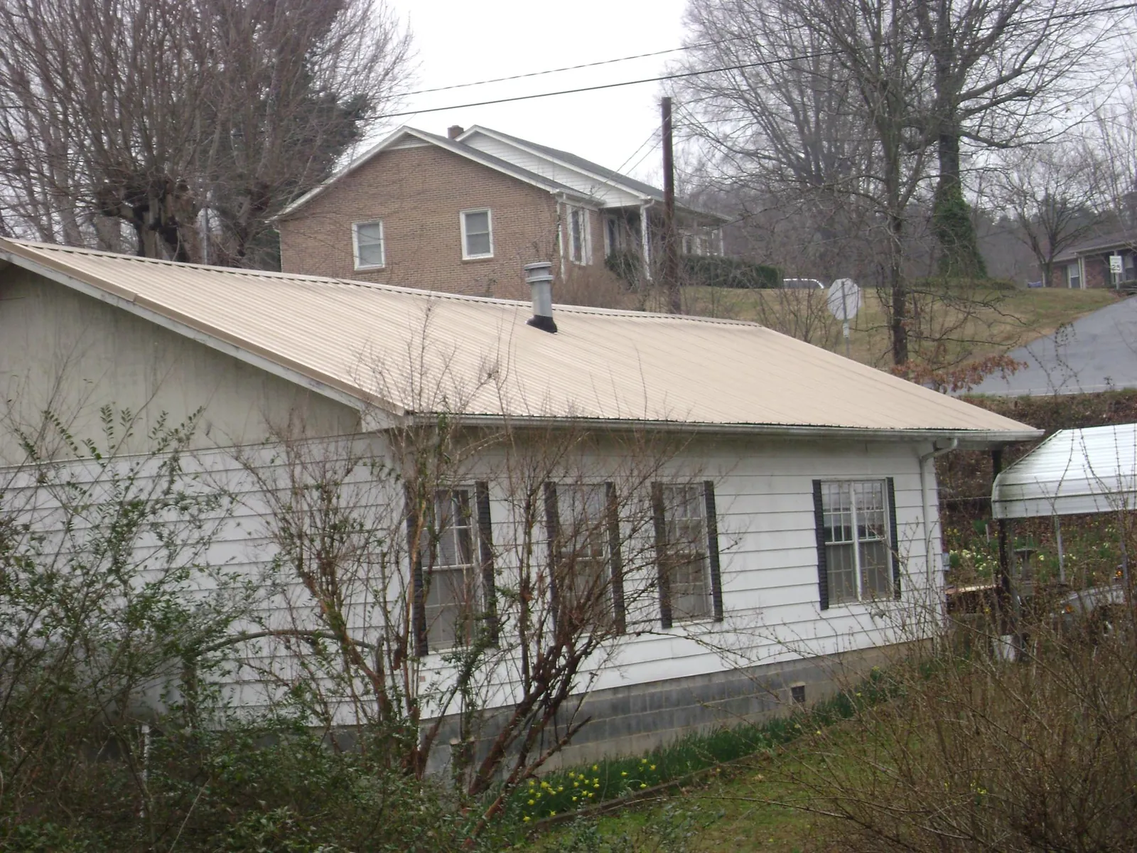 Tan metal roof on a white sided house set into a hillside — Commercial Roofing by Roofing Brothers in Havre De Grace